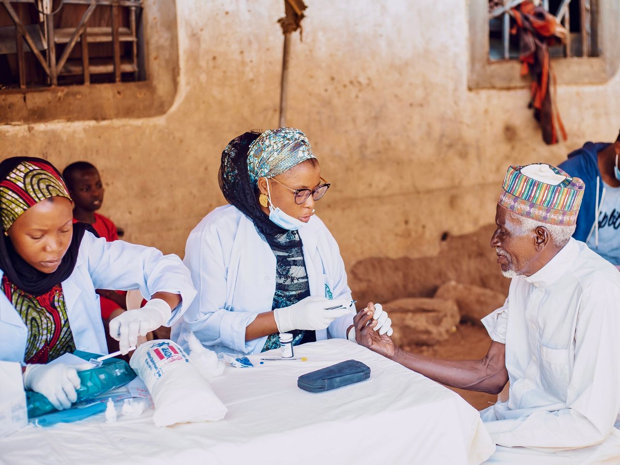 hero-img-01 Healthcare workers assisting elderly man during community outreach in Kaduna, Nigeria.