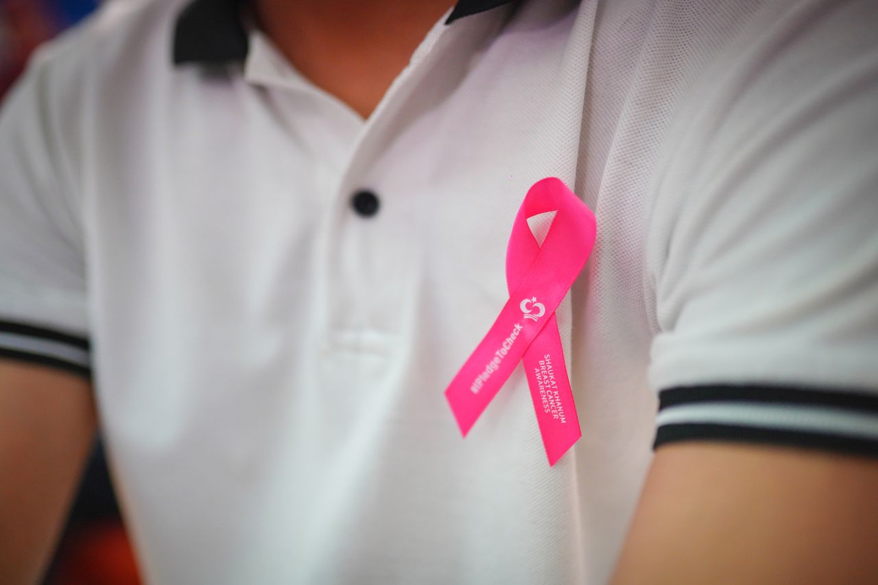 services-03 Close-up of a person wearing a pink ribbon for breast cancer awareness and support.