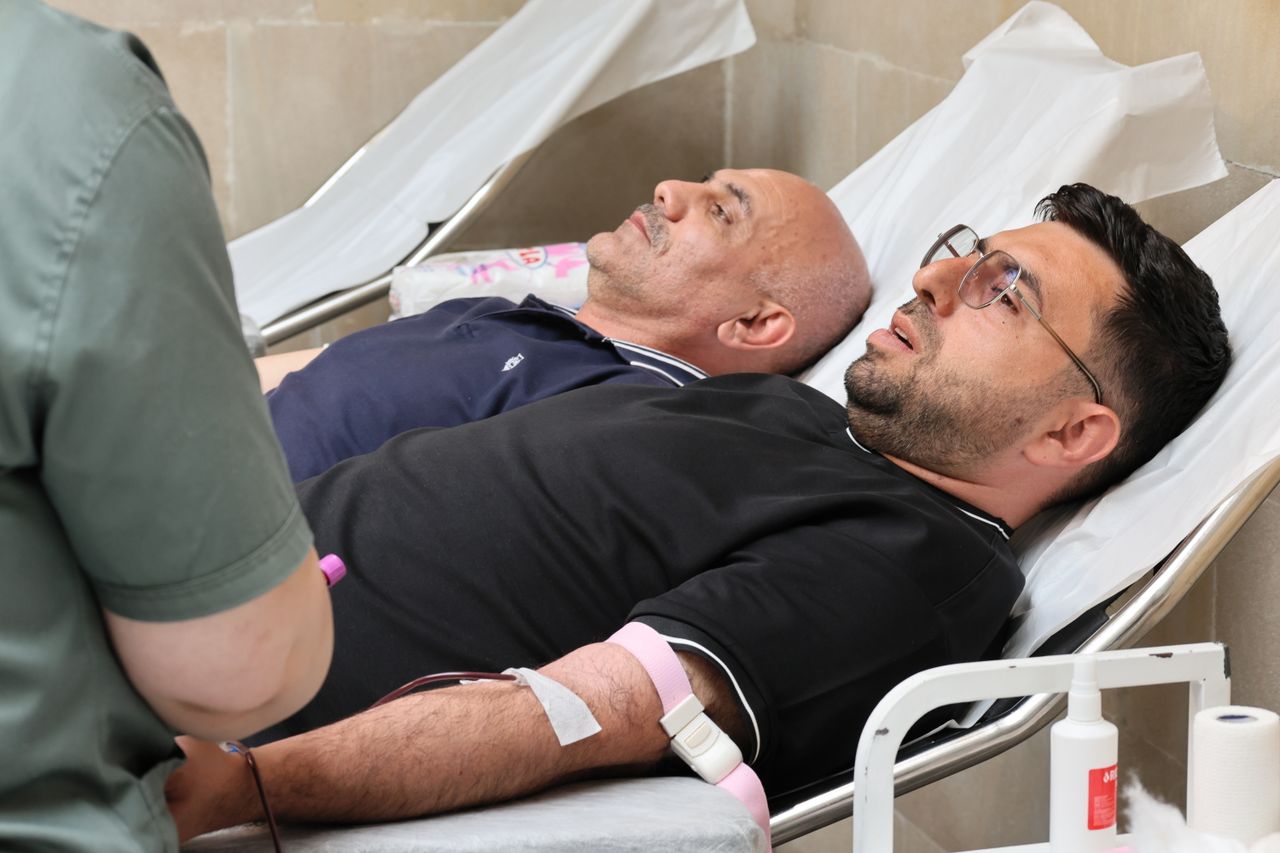 services-02 Two men are lying on medical beds while donating blood at a clinic.