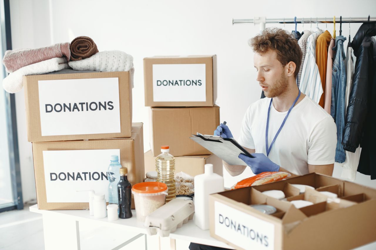 gallery-1 A man organizing donation boxes filled with clothes and food items at an NGO office.