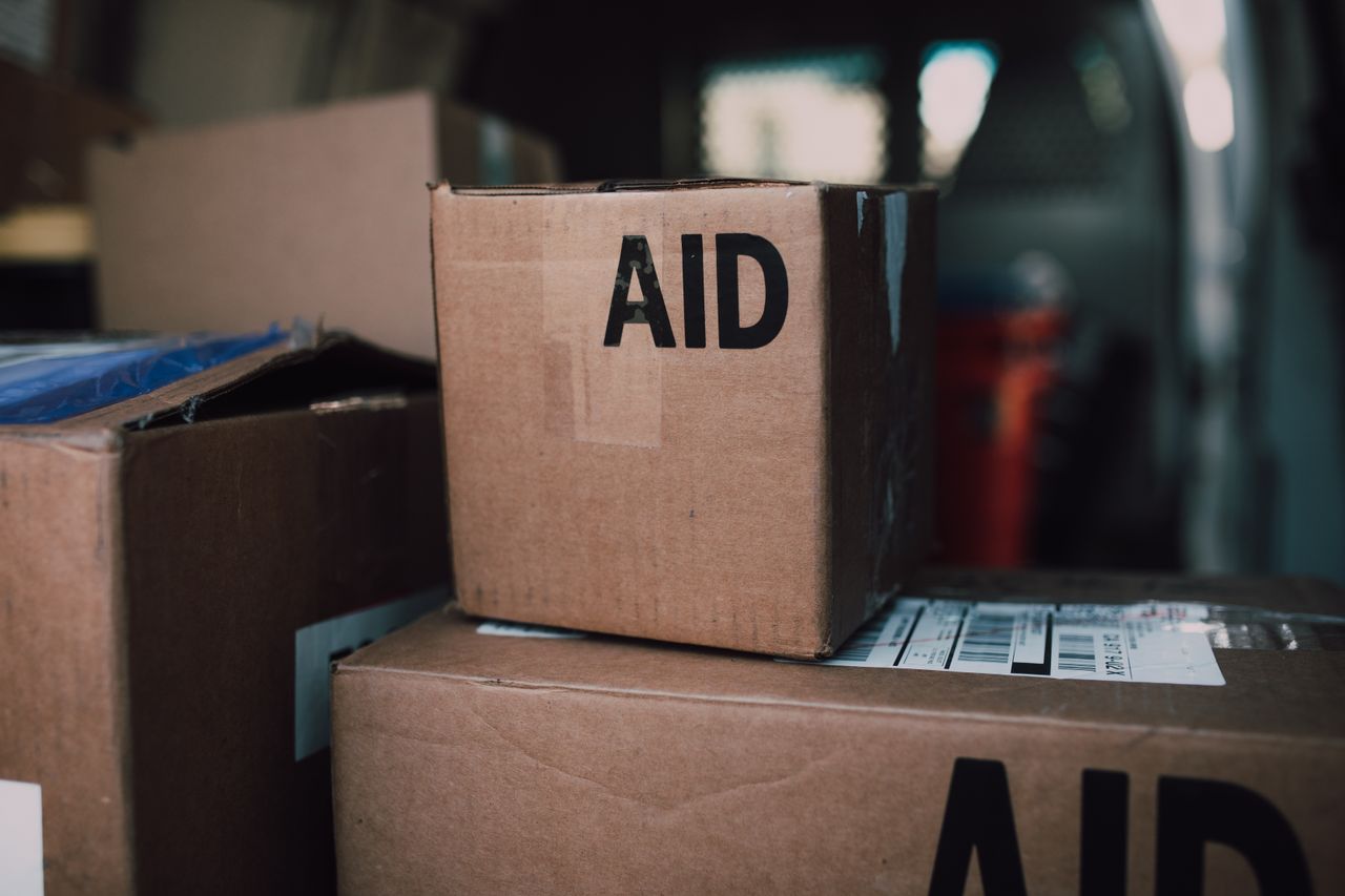heros-img Stacked aid boxes ready for distribution in a delivery vehicle.
